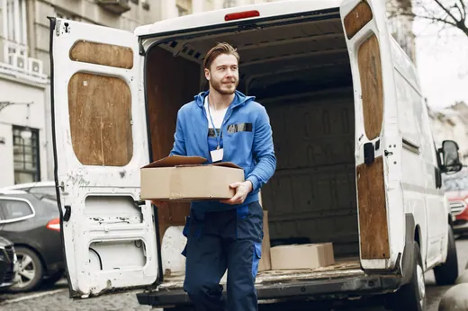 Déménageur portant un carton devant une camionnette stationnée dans une rue