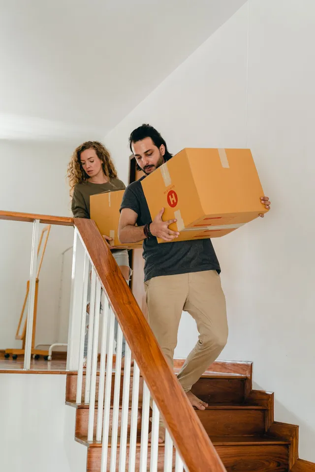 Couple portant un grand carton de déménagement dans un escalier