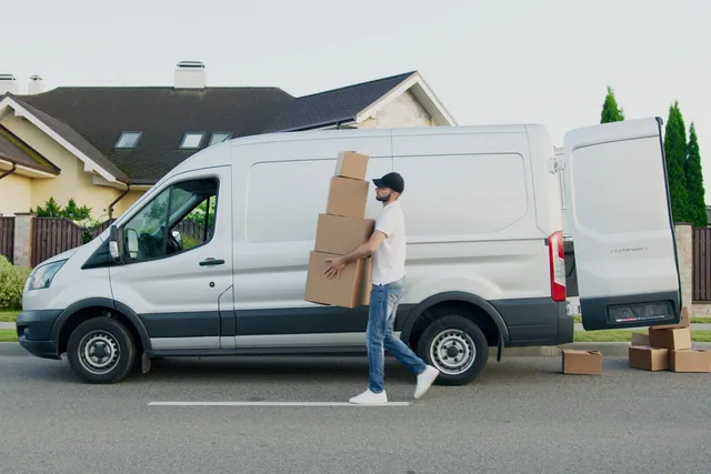 Déménageur portant des cartons devant une camionnette stationnée dans une rue résidentielle